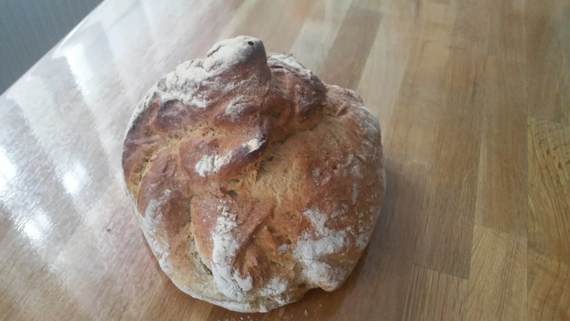 Rustikaler Brotlaib mit Mehlkruste auf einem Holztisch